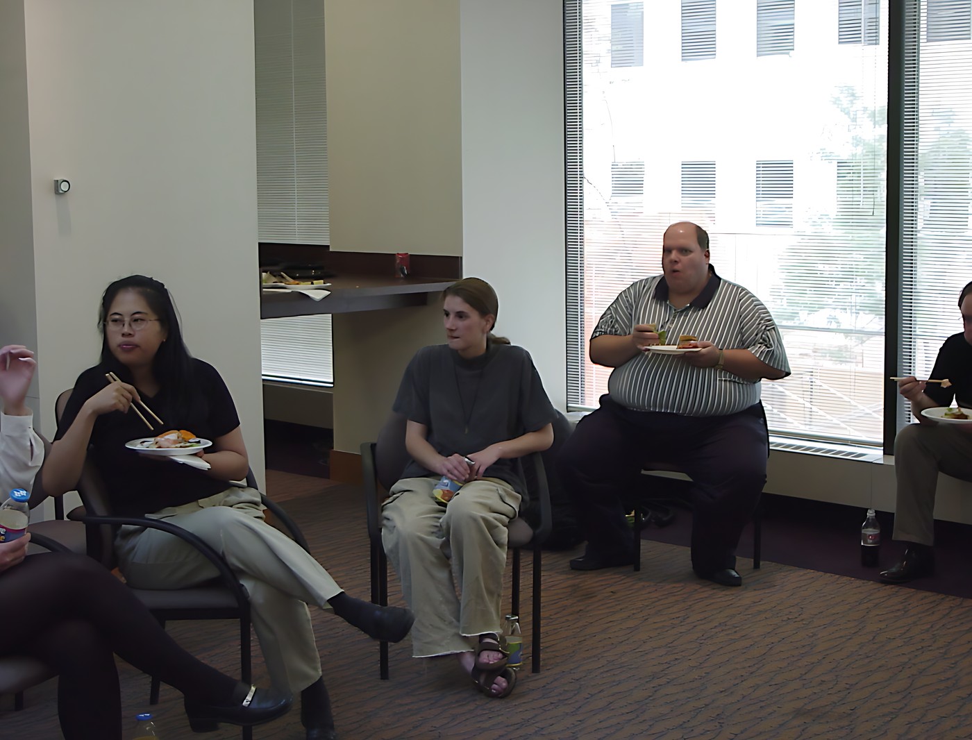 Group of five people sitting in a circle in a room with large windows